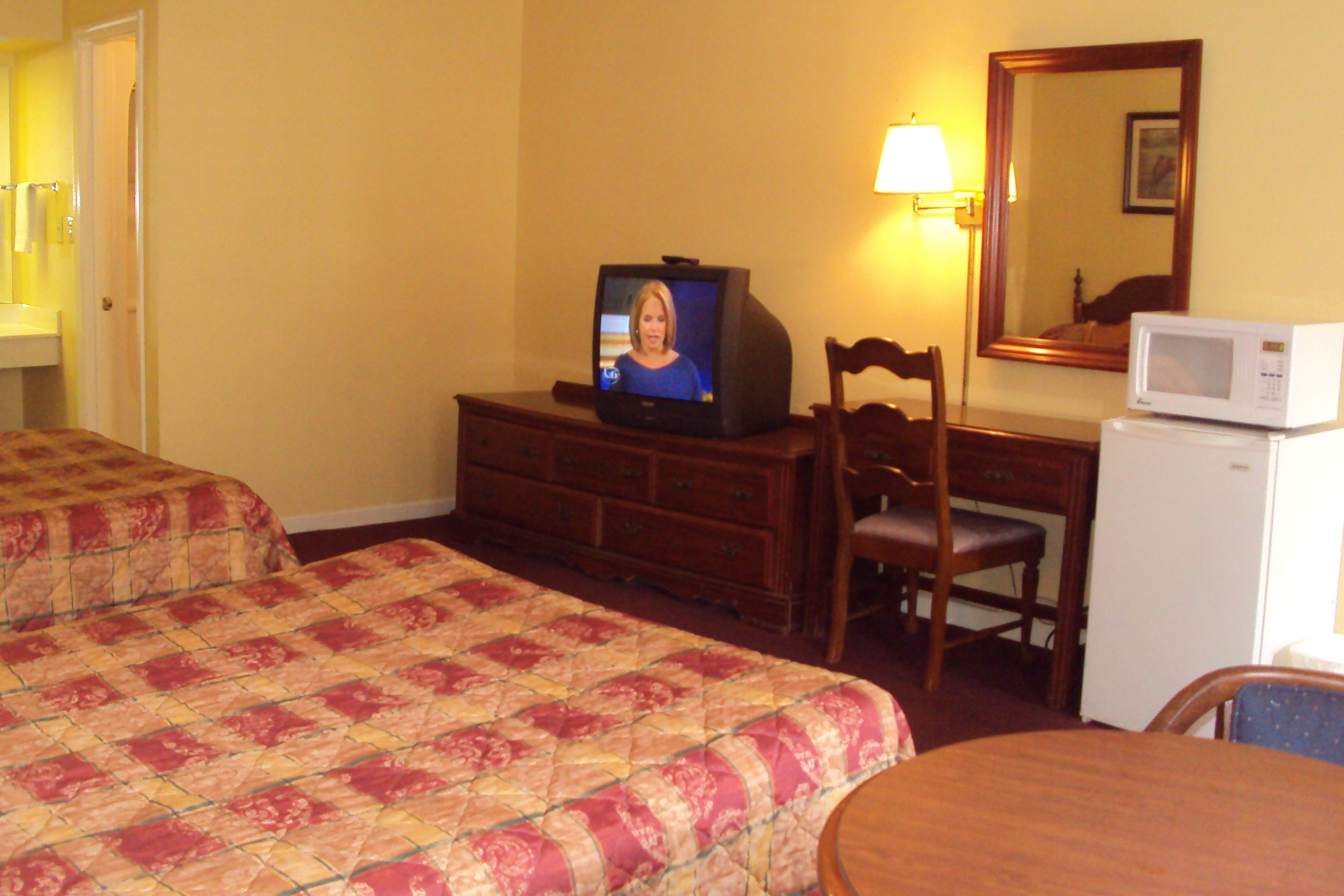 A hotel room with two beds, a television, a desk with a chair, a microwave, and a mirror.