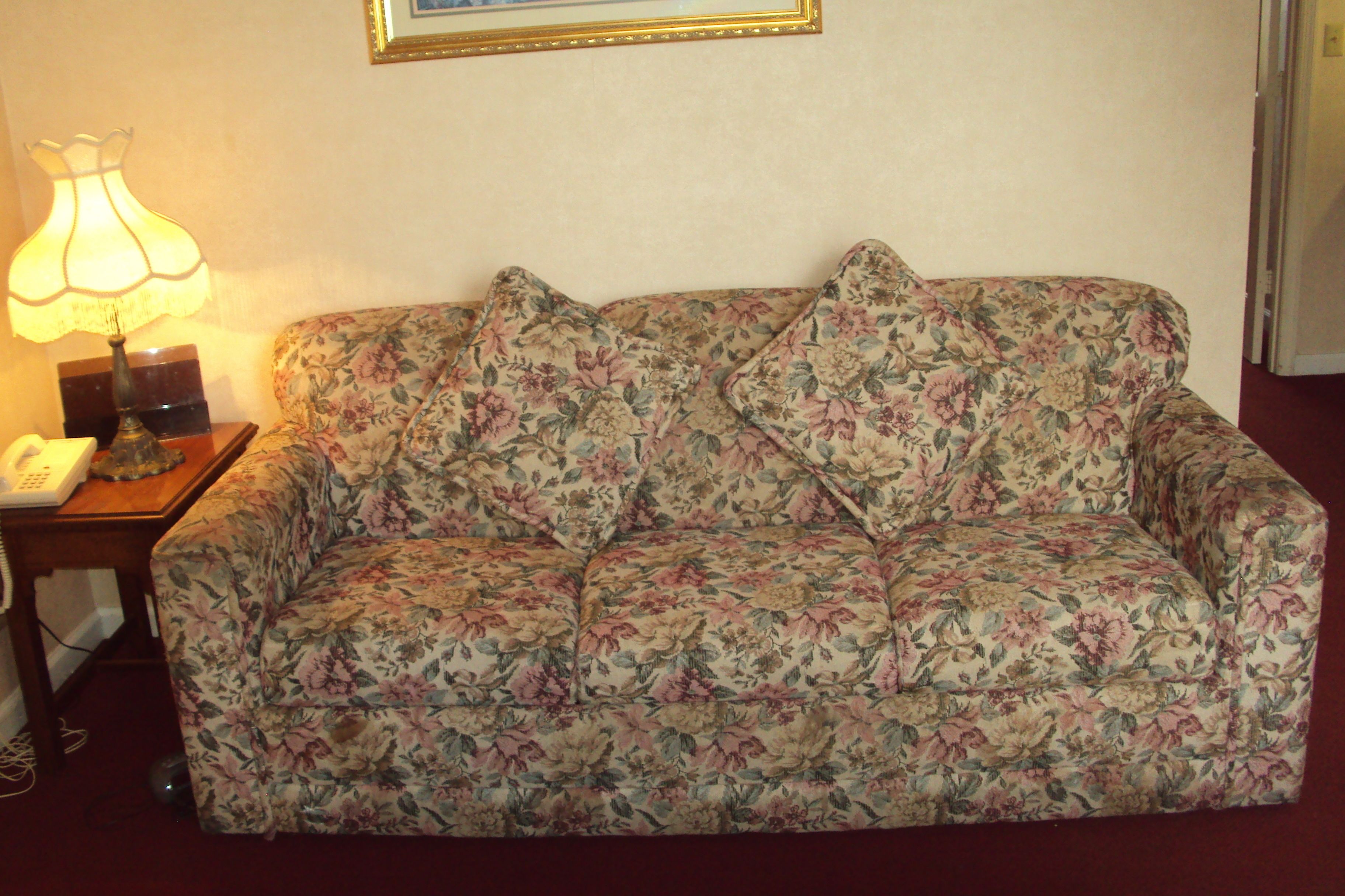 A floral-patterned sofa with a telephone and lamp on a side table.
