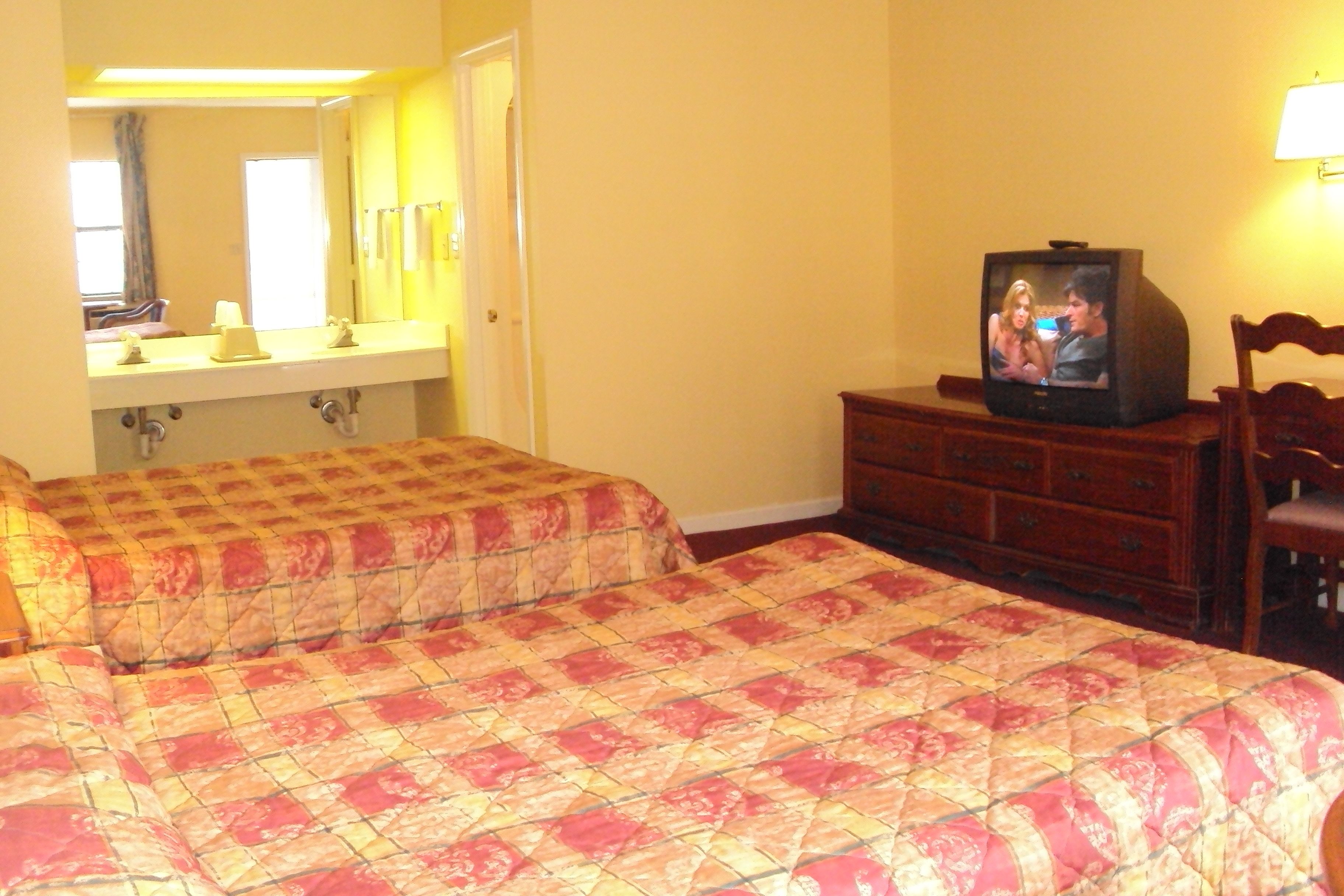 A hotel room with two beds, a television, a dresser, and a mirror.