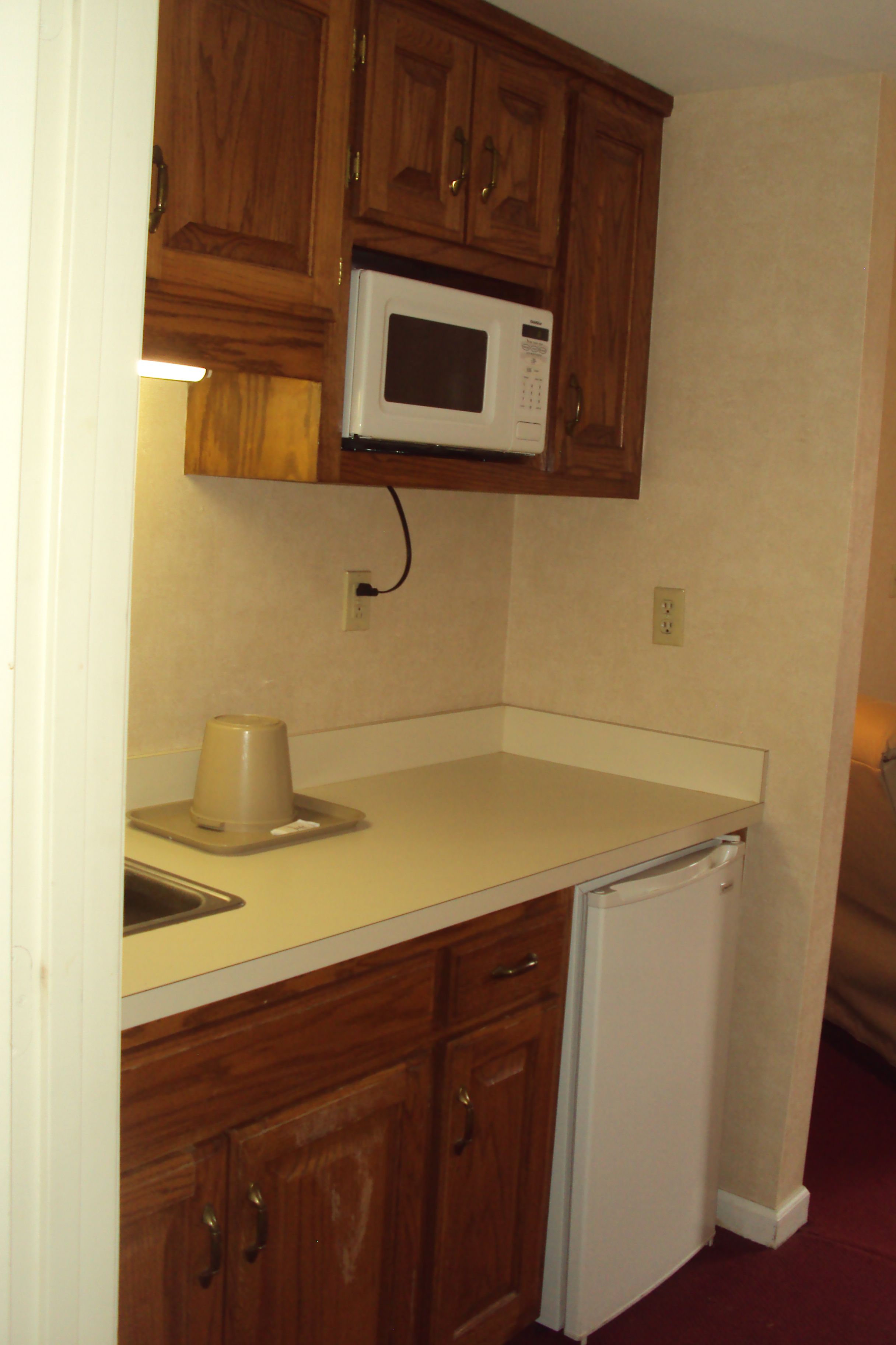 A compact kitchen with wooden cabinets, a microwave, a coffee maker, and a dishwasher.
