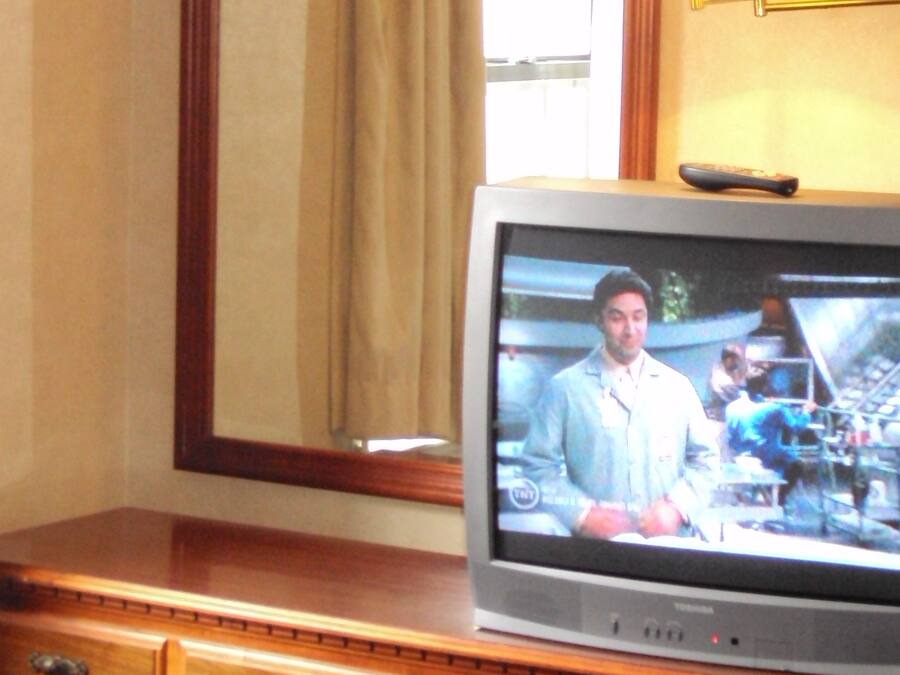 A television on a wooden dresser with a mirror above it.