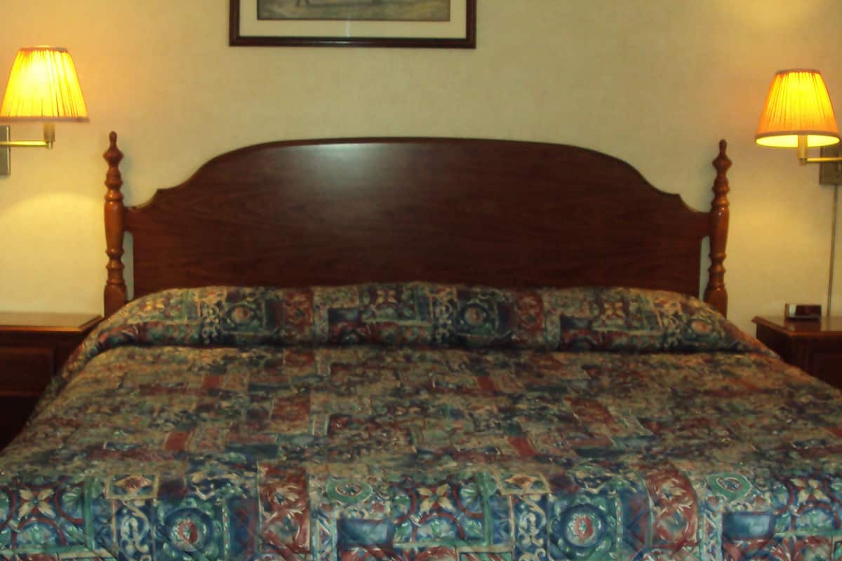 Ein Bett mit gemustertem Überwurf, zwei Nachttischlampen und ein gerahmtes Bild an der Wand.