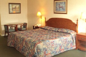 Una habitación de hotel con una cama grande, una mesita de noche, una silla y un escritorio.