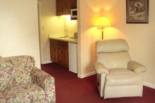 Una sala de estar con un sofá floral, un sillón color beige y una cocina al fondo.