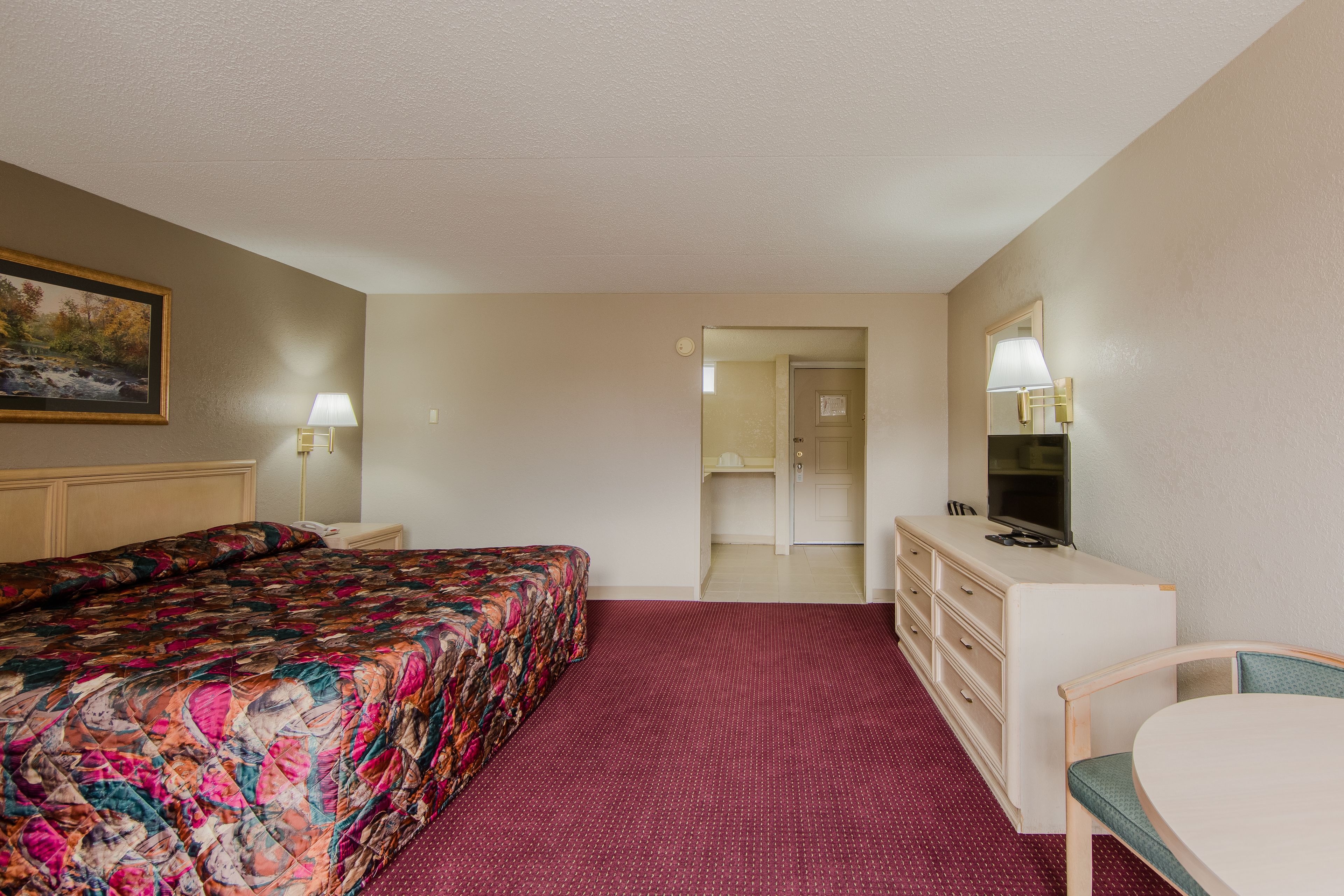 Habitación de hotel con cama, escritorio, silla, televisor y un cuadro en la pared.