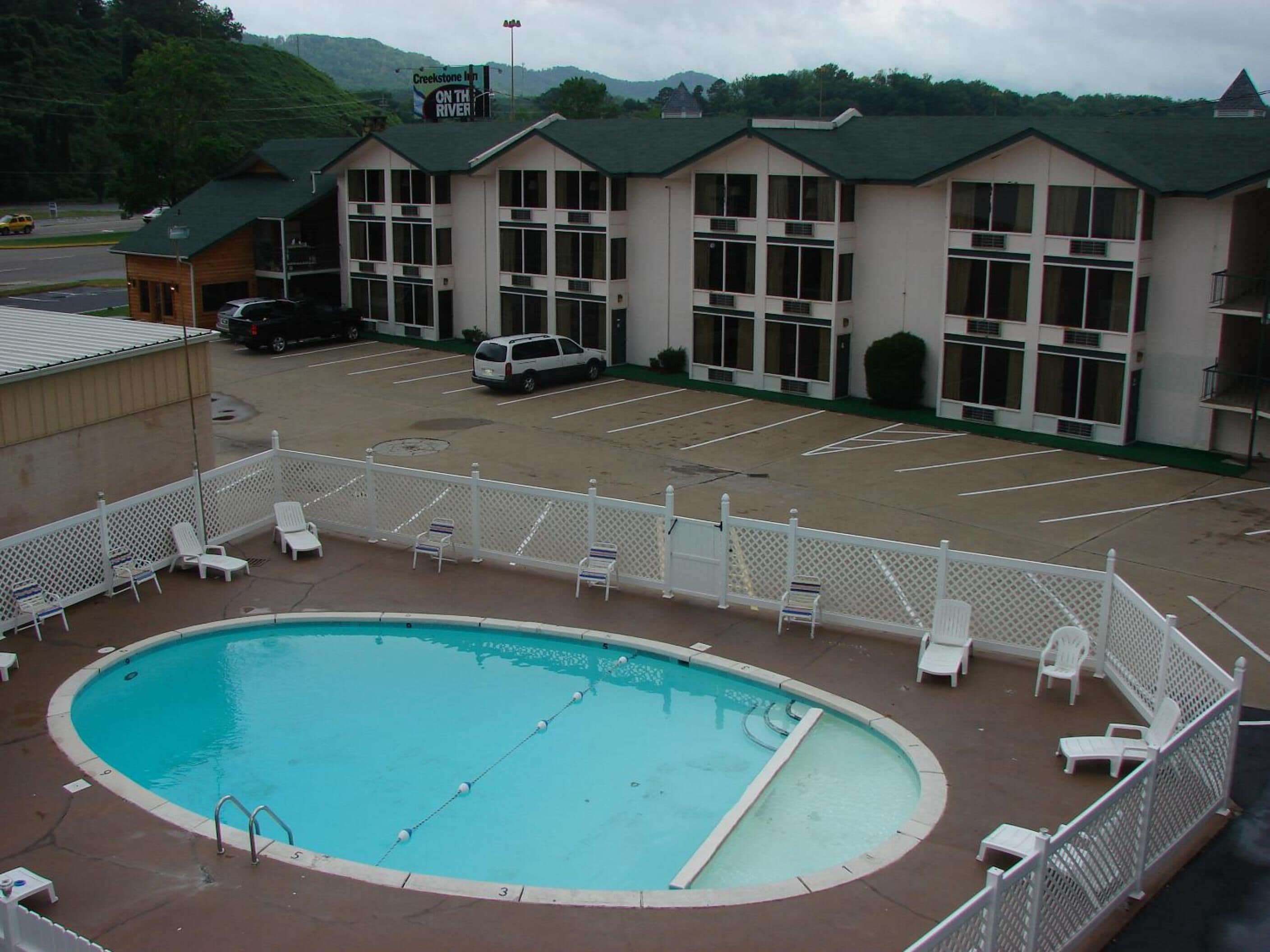Un hotel con piscina, estacionamiento y un edificio de varios pisos con tejado verde.