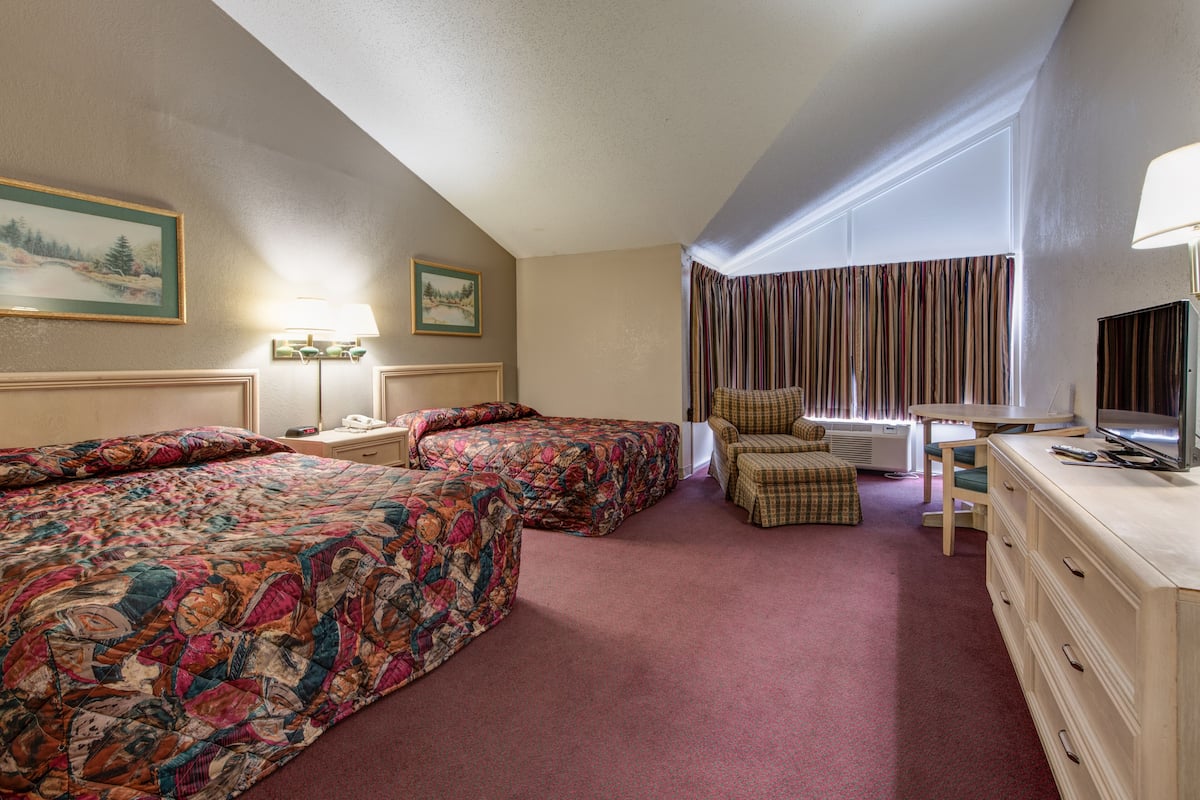 Quarto de hotel com duas camas, uma escrivaninha, uma cadeira, uma televisão e uma janela com cortinas.