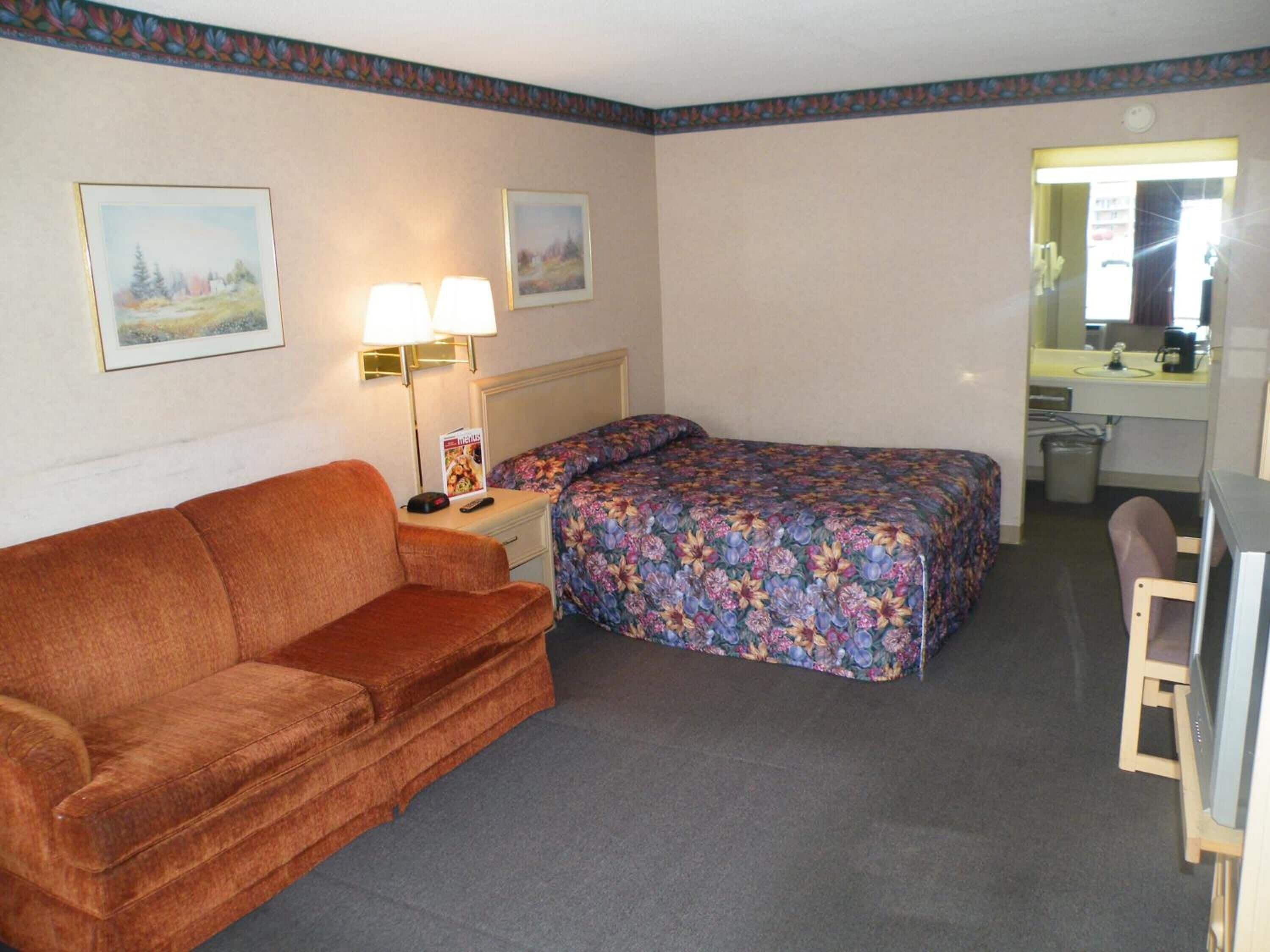 Une chambre d’hôtel comprenant un lit, un canapé, une table de chevet, une lampe, un miroir et un téléviseur.