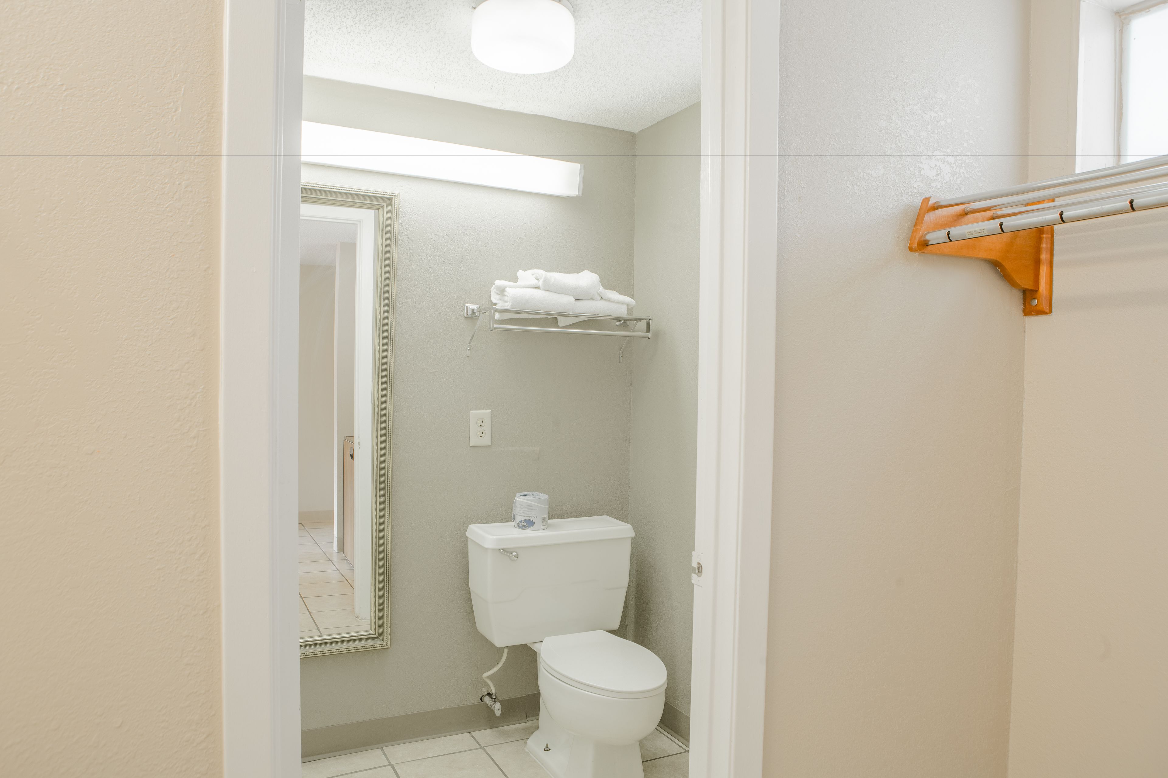 A small, clean bathroom with a toilet, a towel rack, and a shelf above the toilet.