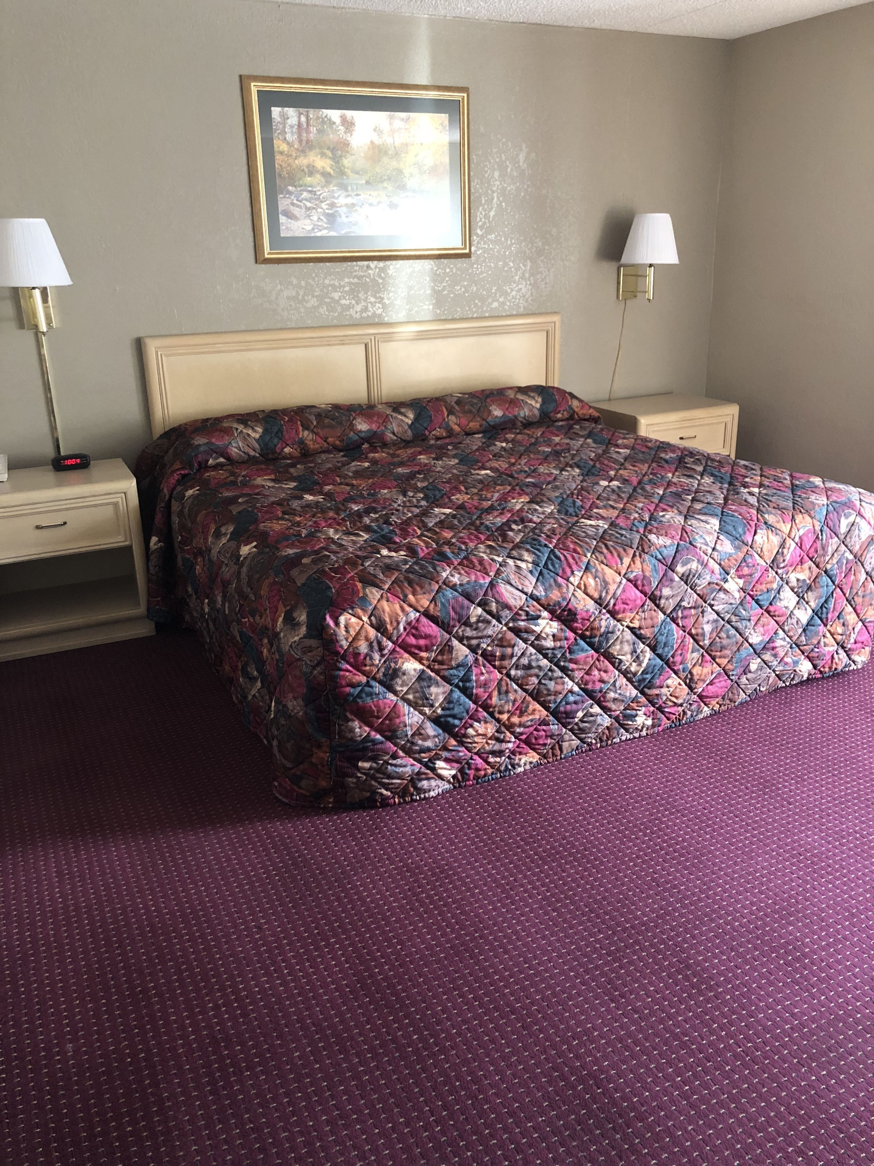A hotel room with a large bed, two bedside tables, a nightstand, and a wall-mounted lamp.