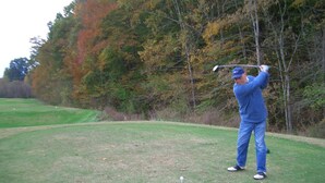 Une personne vêtue de bleu jouant au golf sur un terrain verdoyant, avec des arbres en arrière-plan.