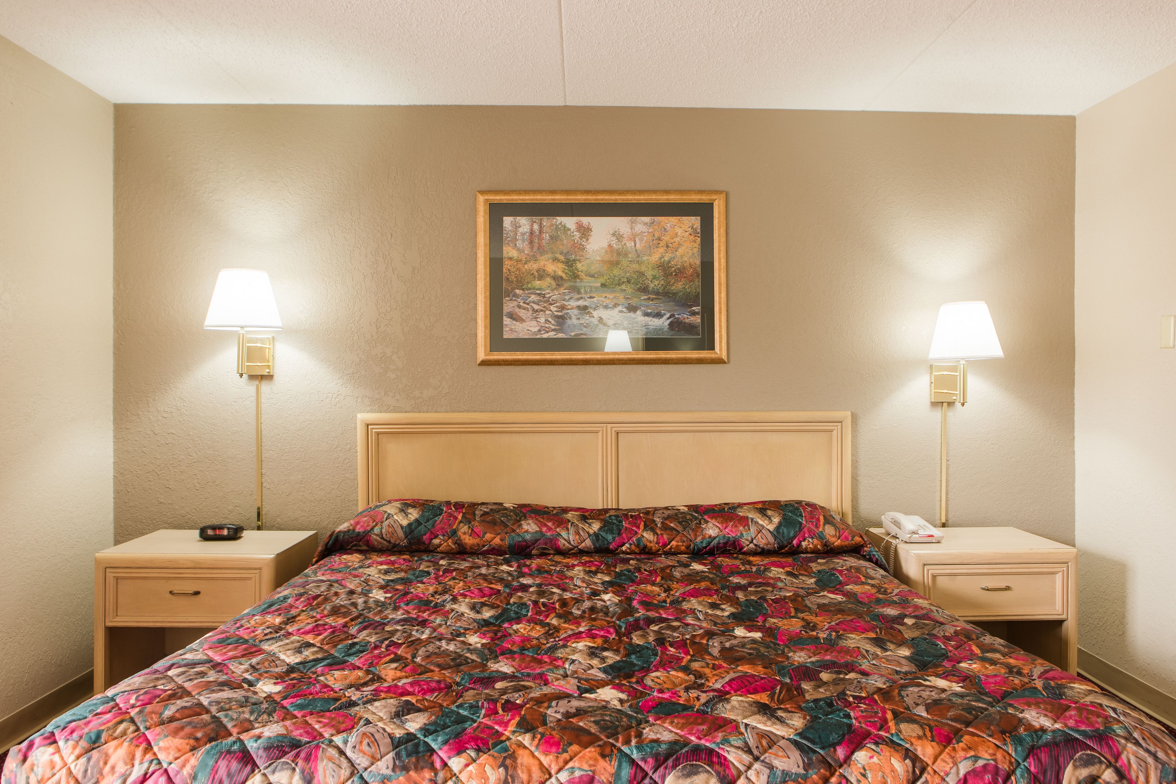 A hotel room with a large bed, two bedside tables, a nightstand, a lamp, and a framed picture on the wall.
