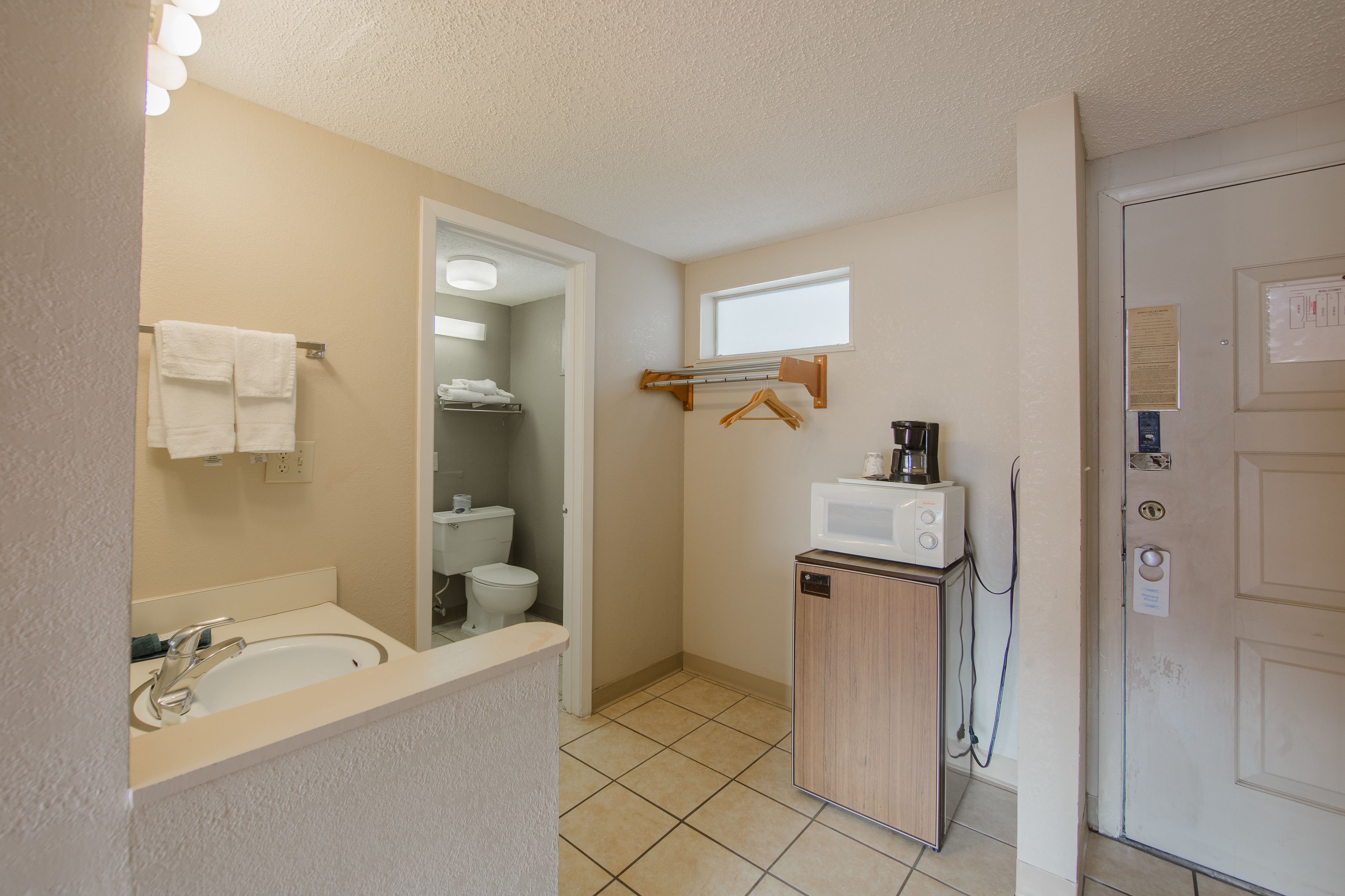 A compact bathroom with a sink, mirror, towel rack, toilet, and a small cabinet with a microwave.