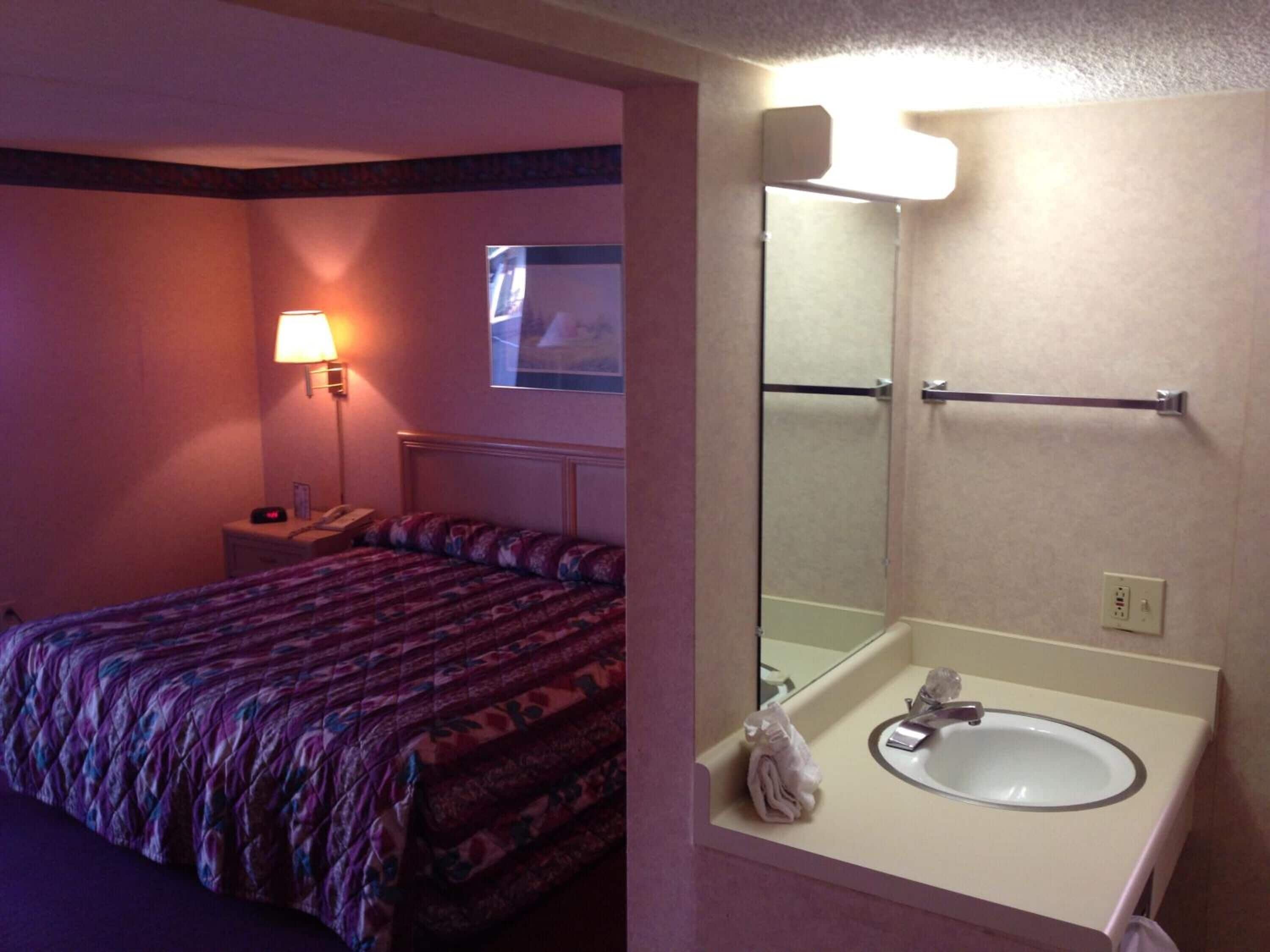 A hotel room with a bed, a bedside lamp, a mirror, and a sink.