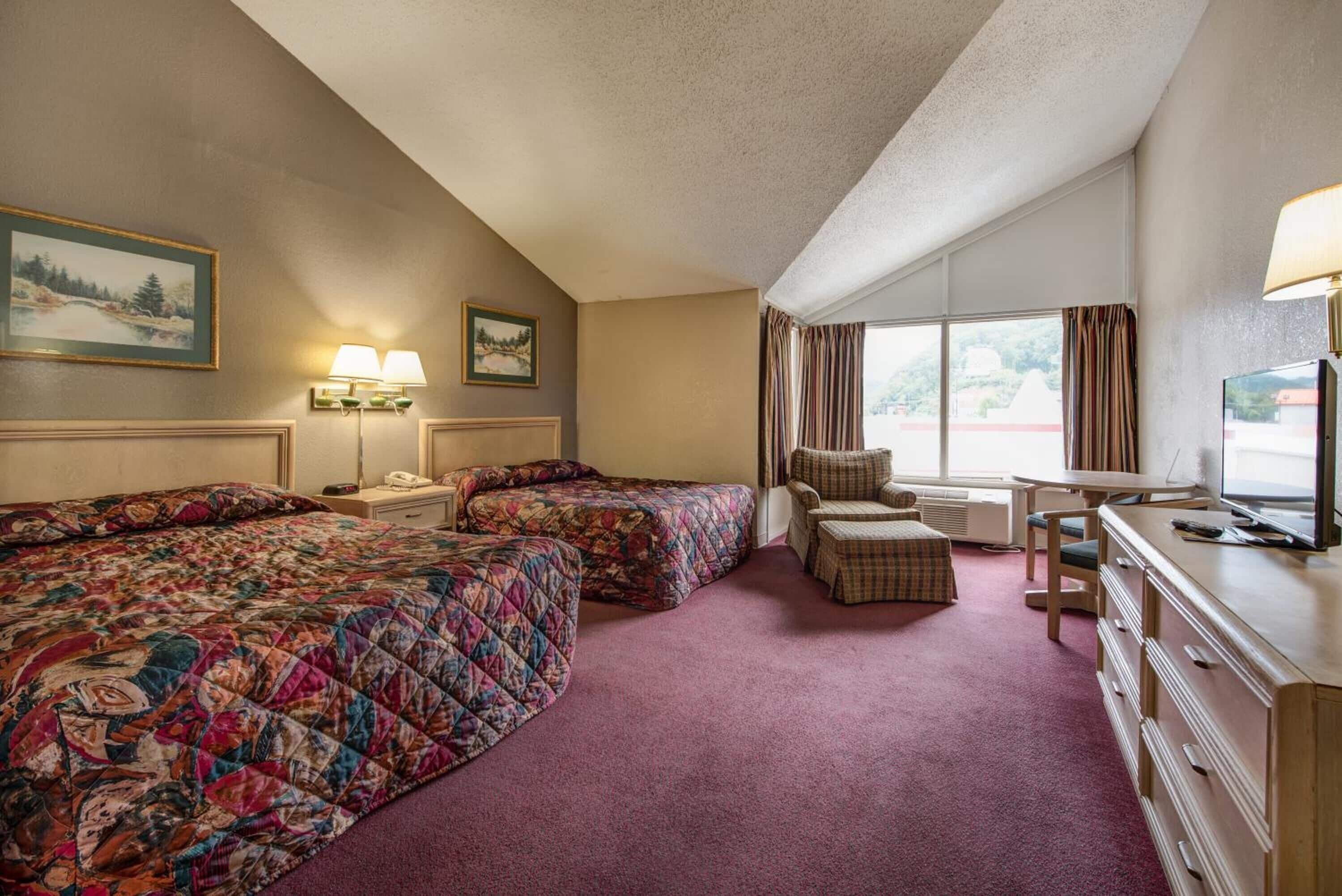 A hotel room with two beds, a desk, a chair, a television, and a window with curtains.