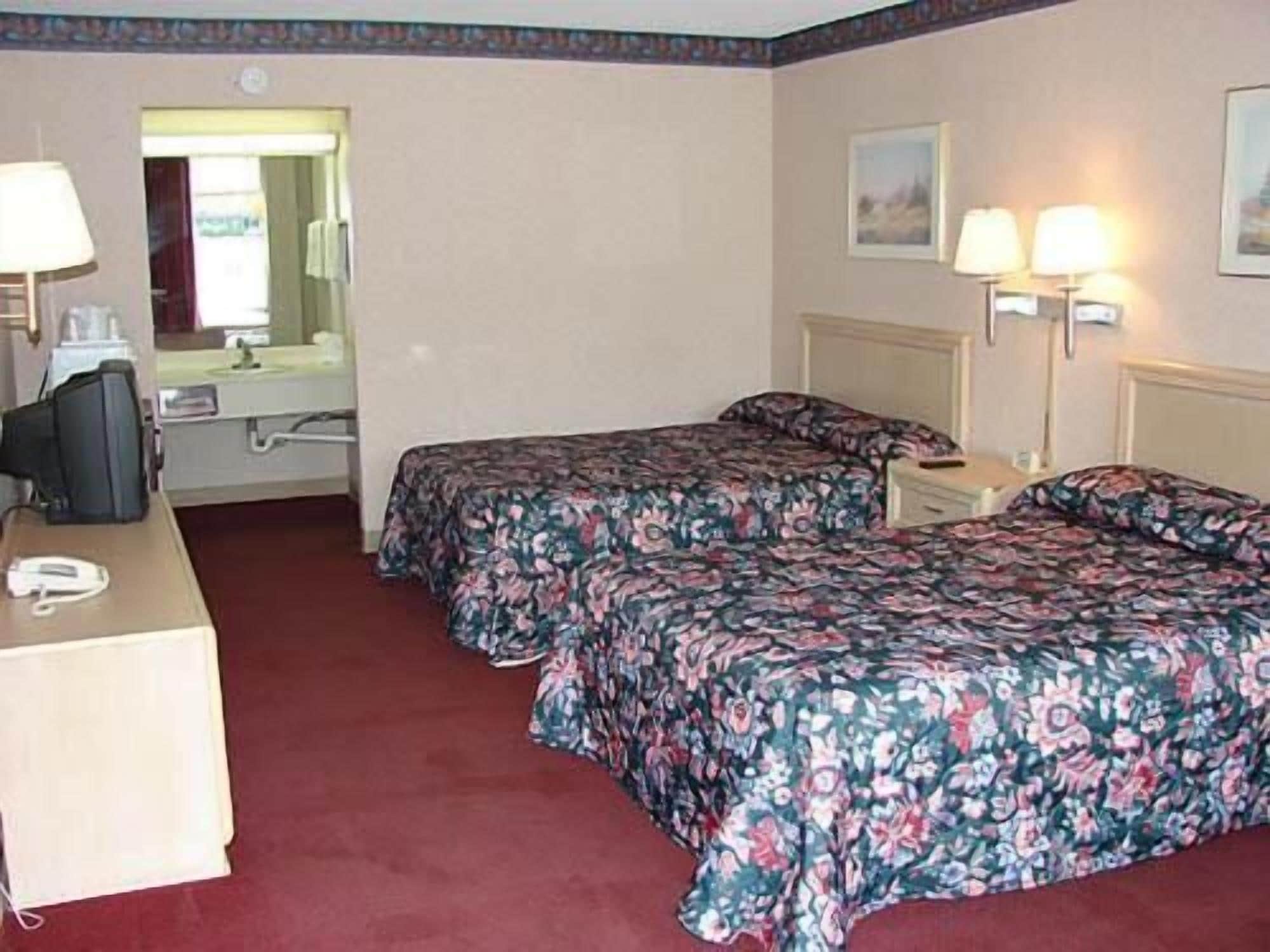 Habitación de hotel con dos camas, un escritorio, una silla, un teléfono y dos lámparas fijadas a la pared.