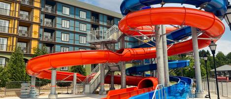 A water park with multiple slides, a pool, and a building with balconies in the background.