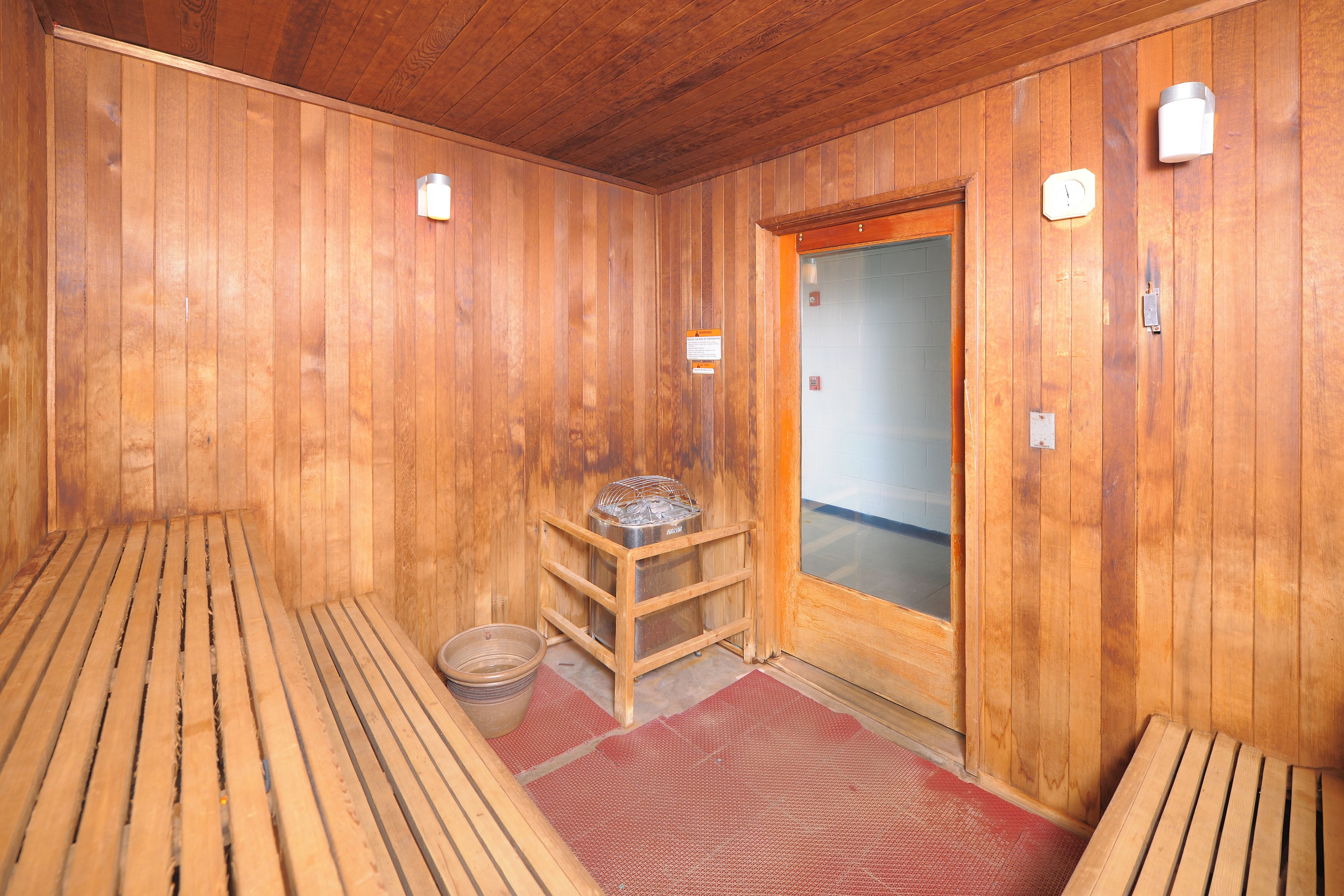 A wooden sauna room with benches, a heater, and a glass door.