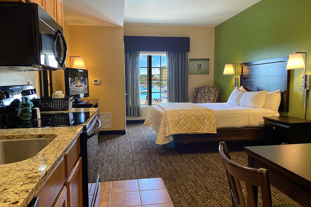 Una habitación de hotel con cama, escritorio, kitchenette y vista a una piscina.