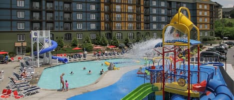 Un hotel con un amplio espacio de piscina que incluye toboganes, estructuras de juegos acuáticos y sillas de descanso.