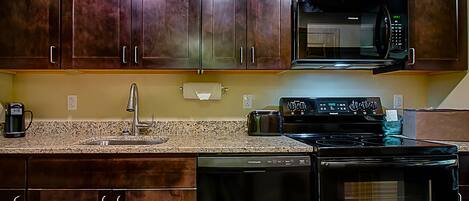 A kitchen with dark wooden cabinets, a stainless steel sink, a microwave, a toaster, and a Frigidaire dishwasher.