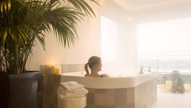 A spa bathroom with a bathtub, a potted plant, and candles. - Hotel Rheinpark Rees (Rees)