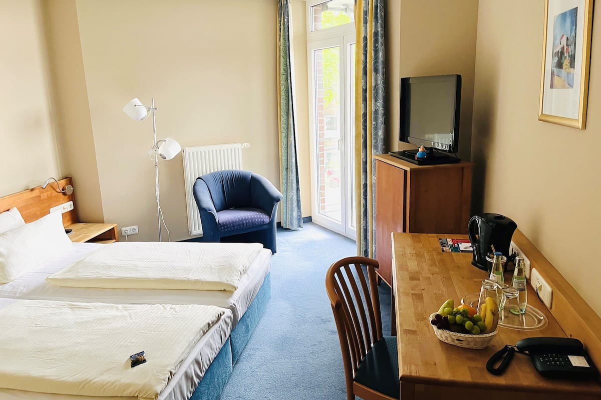 Habitación de hotel con dos camas, un escritorio con teléfono, una silla, televisor y ventana con cortinas.