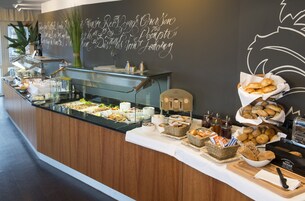 Balcão de buffet com diversos alimentos, uma máquina de café e uma parede decorativa com texto.