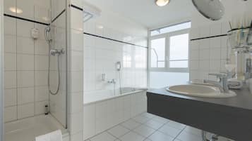 Un baño moderno con ducha envuelta en vidrio, bañera, lavamanos y un espejo grande.