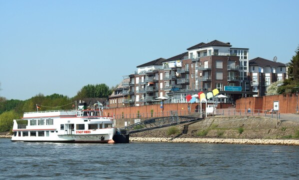 A riverboat docked near a waterfront with a multi-story building in the background.