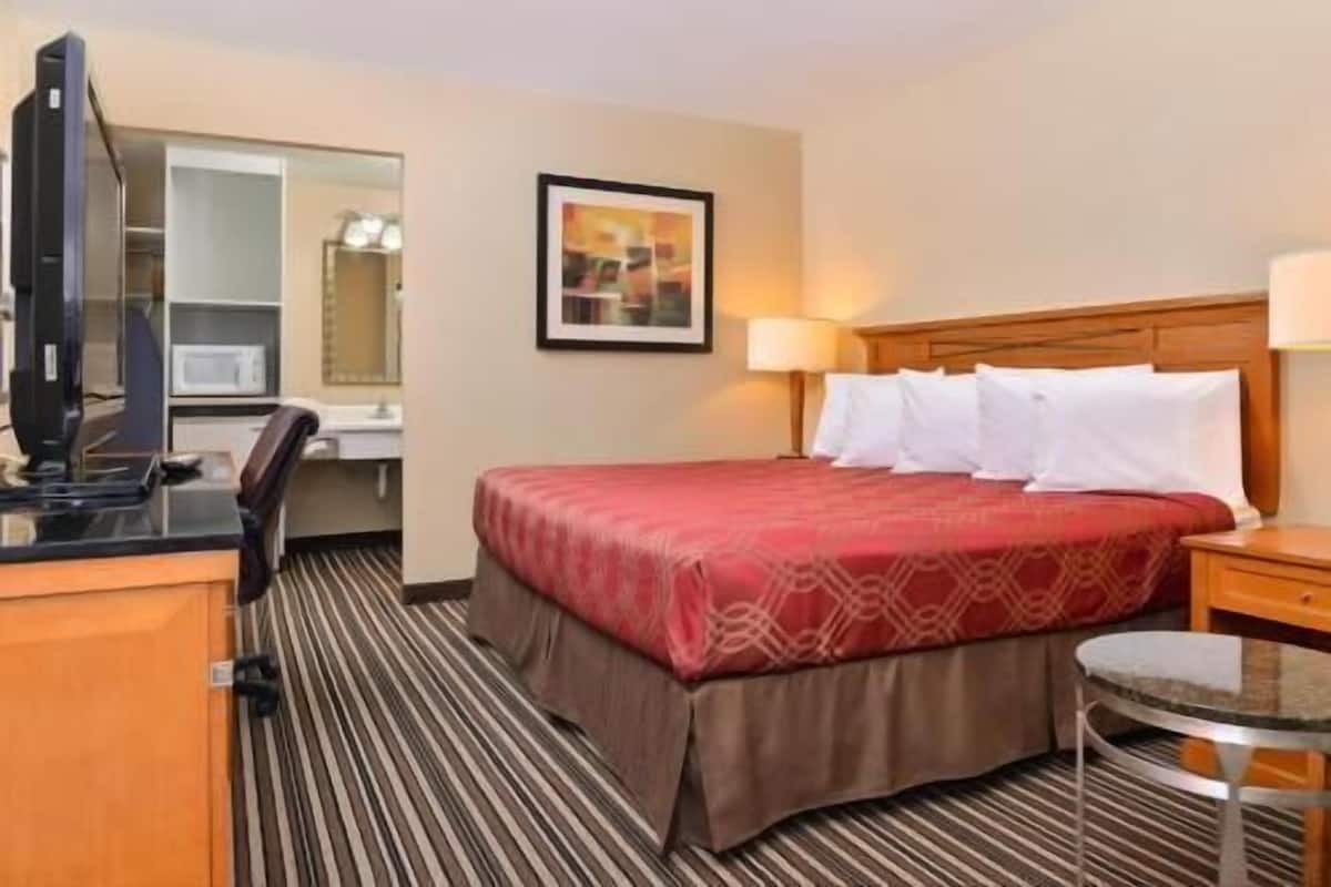 Une chambre d’hôtel avec un lit, un bureau équipé d’un ordinateur, une chaise, une lampe et une petite table.