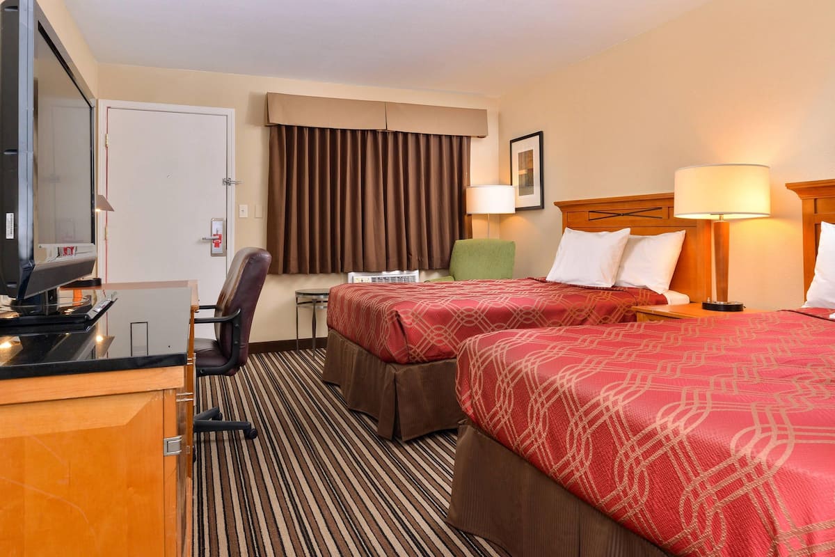 Une chambre d’hôtel avec deux lits, un bureau, une chaise, une télévision et une fenêtre avec des rideaux.