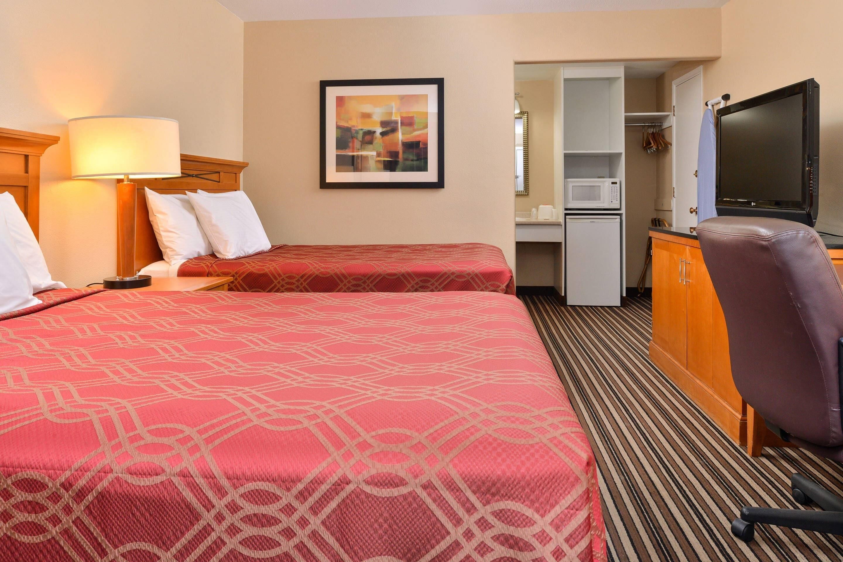 A hotel room with two beds, a desk, a television, a microwave, and a wardrobe.