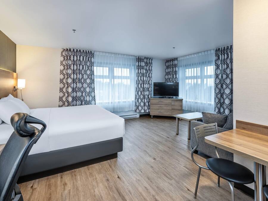 A hotel room with a bed, a desk, a chair, a TV, and patterned curtains.