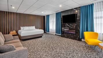 Quarto de hotel com cama, sofá, televisão e lareira.