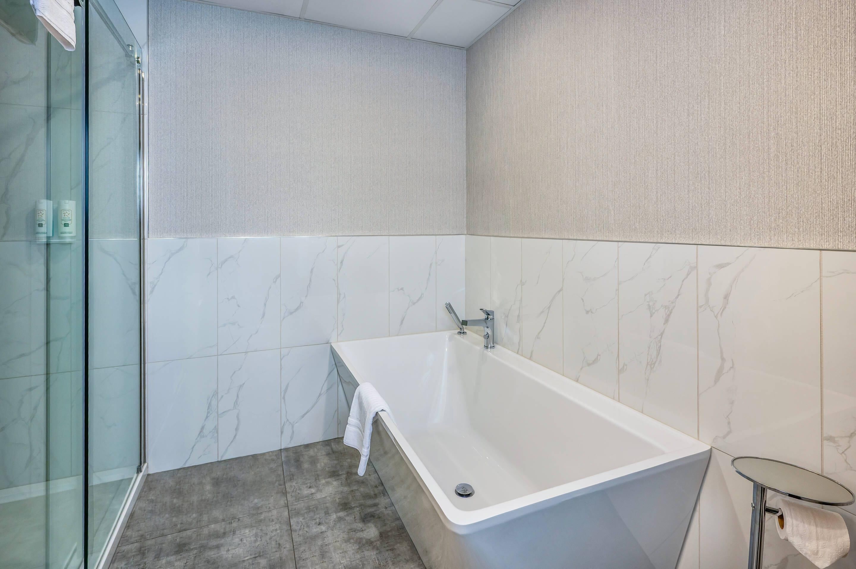 A modern bathroom with a freestanding bathtub, glass shower enclosure, and marble tiles.