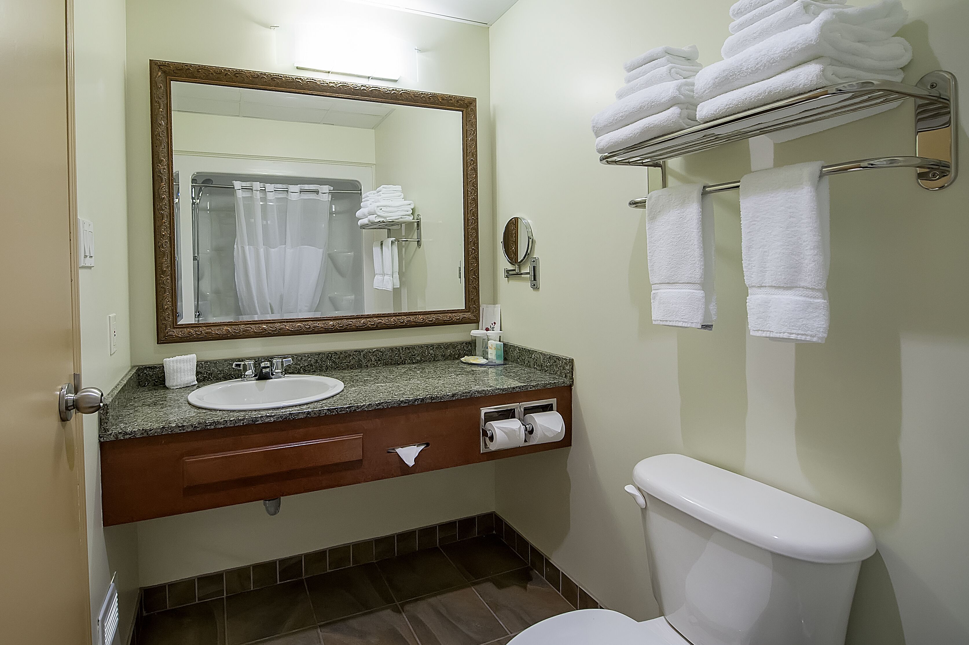 Un baño con lavamanos, espejo, toallero y retrete.