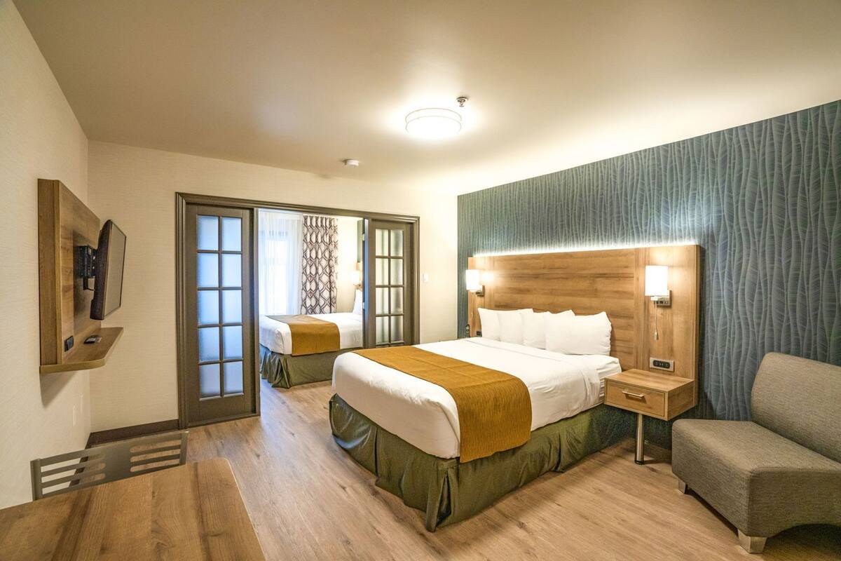 Una camera d'albergo con un letto, una sedia, una scrivania, uno specchio e una porta che dà su un'altra stanza.