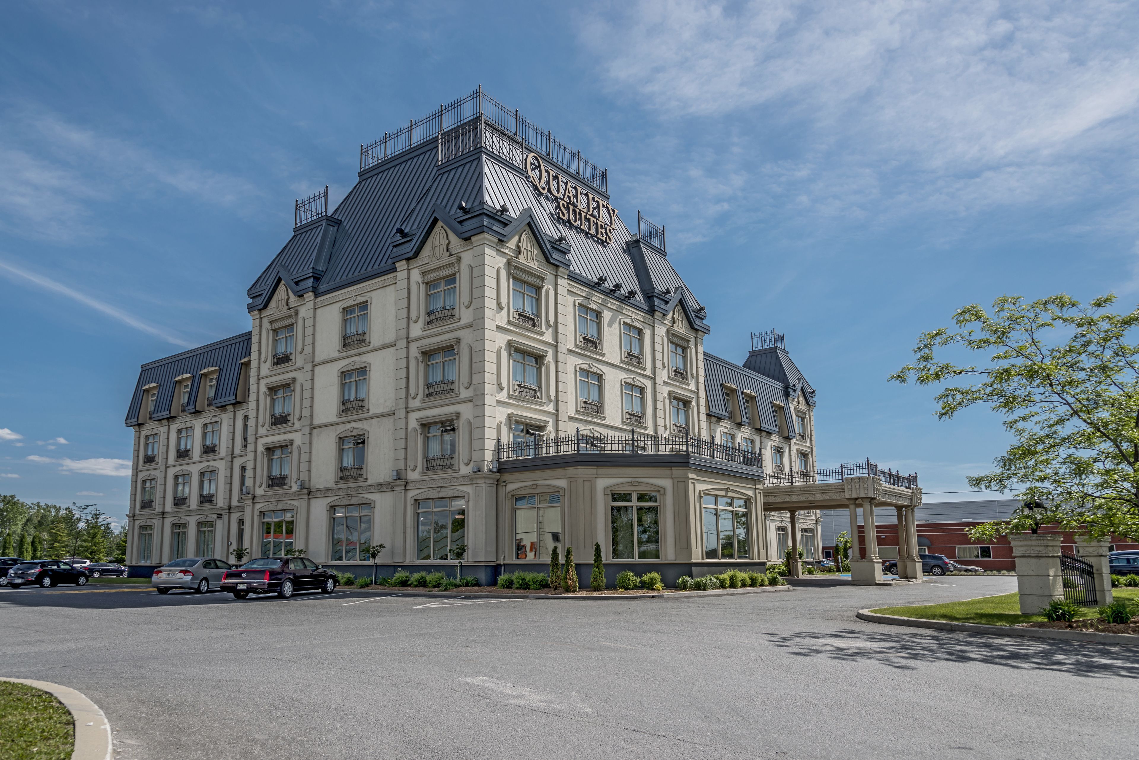 Un grand hôtel à plusieurs étages, doté d’un balcon imposant et d’une enseigne indiquant « Suites Queen ».