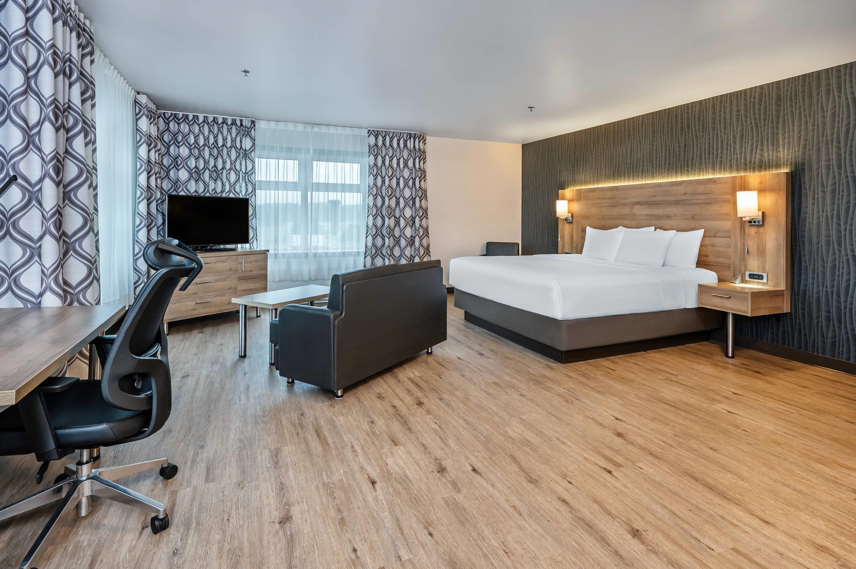A modern hotel room with a large bed, a desk with a chair, a television, and a patterned wall.