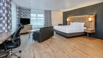 A modern hotel room with a large bed, a desk with a chair, a television, and a patterned wall.