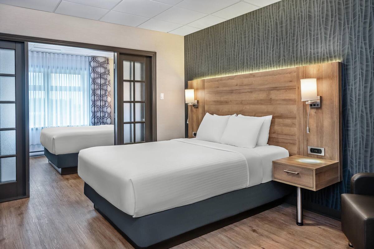 Una camera d'albergo moderna con un grande letto, un comodino con una lampada e vista attraverso una porta in vetro.