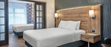 A modern hotel room with a large bed, a bedside table with a lamp, and a view through a glass door.