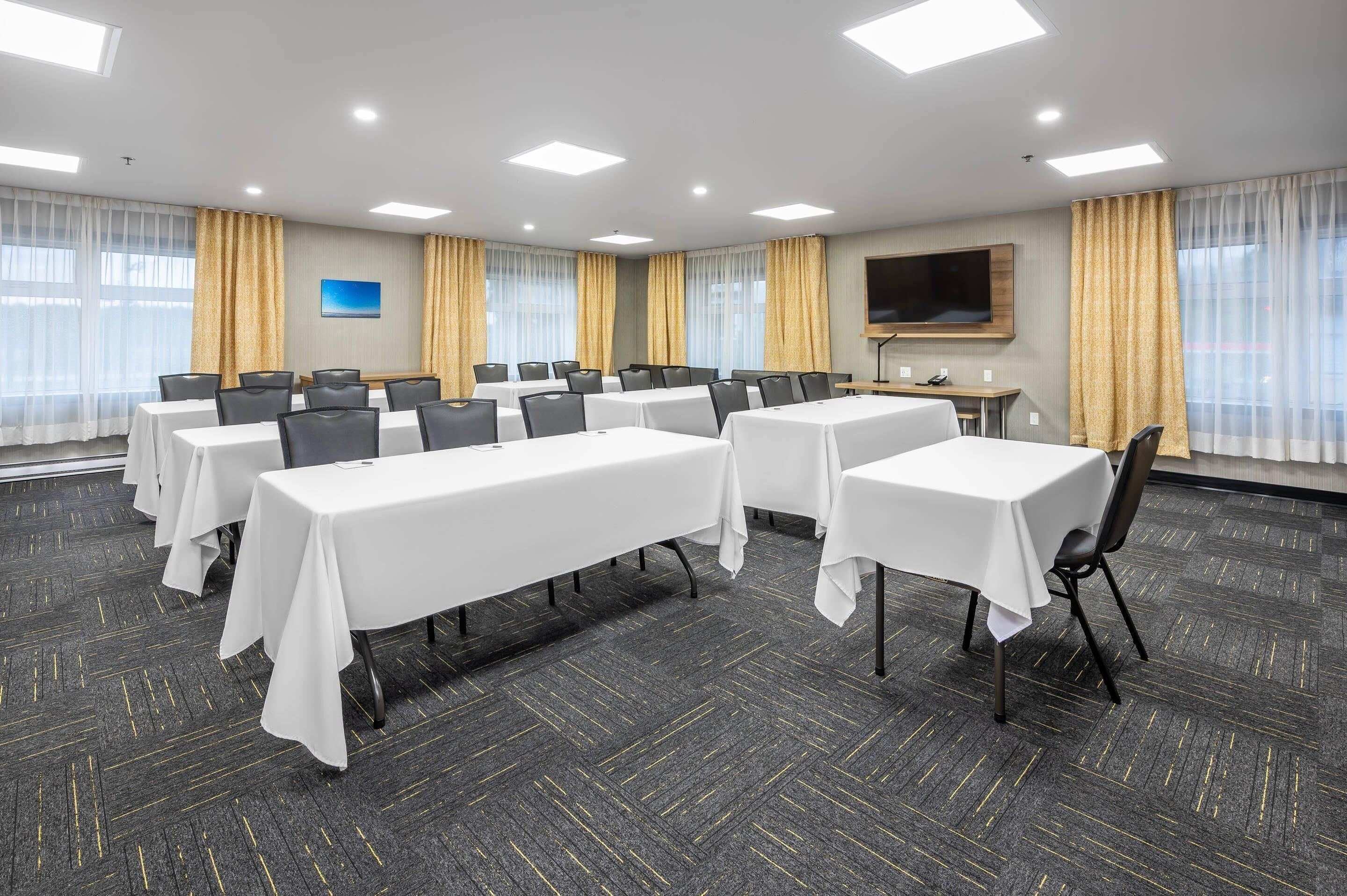 A conference room with multiple tables and chairs, a flat-screen TV, and large windows with curtains.