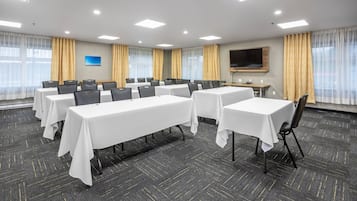 A conference room with multiple tables and chairs, a flat-screen TV, and large windows with curtains.