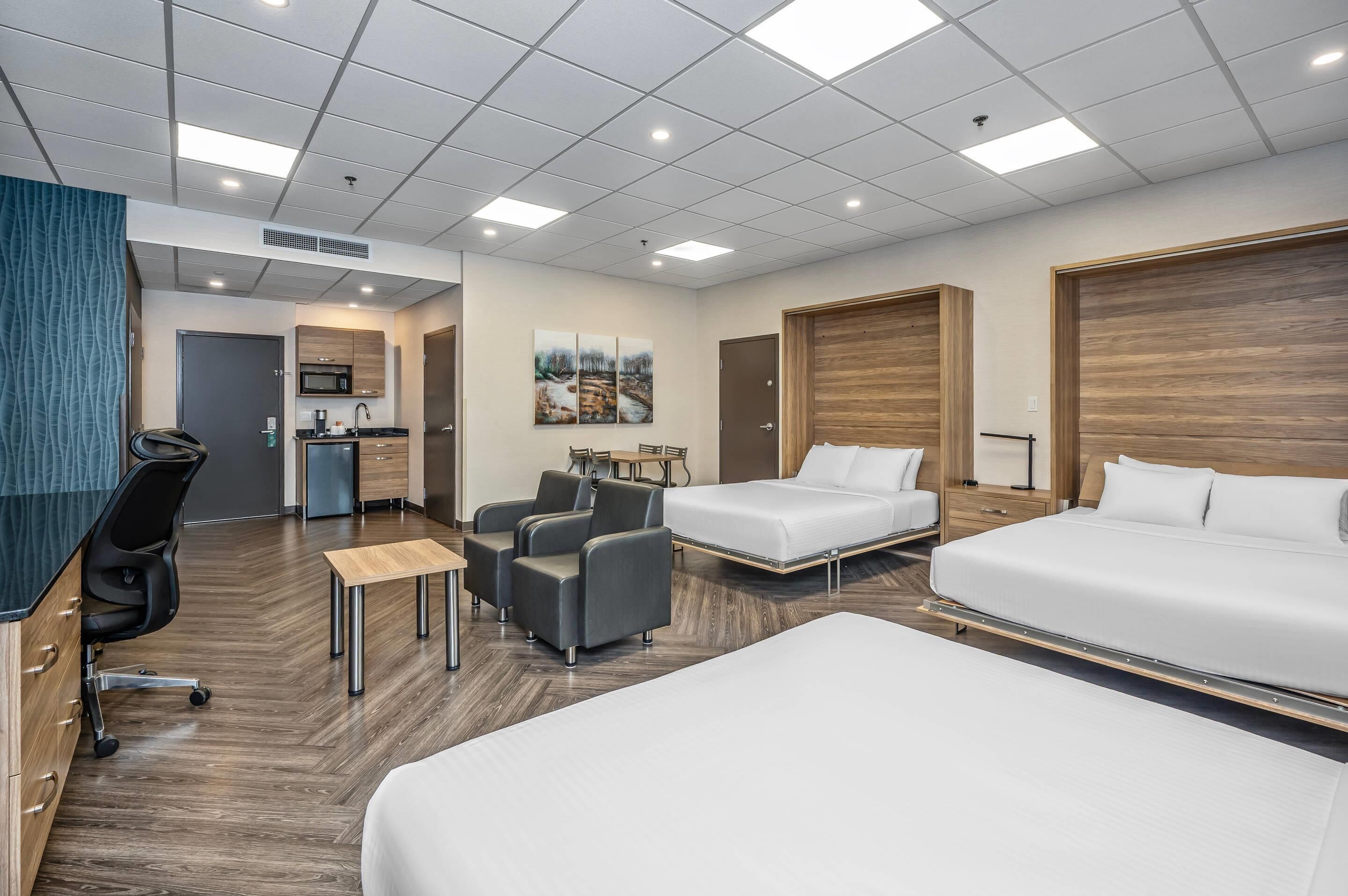 A hotel room with two beds, a desk, a chair, a small table, a microwave, and a sink.