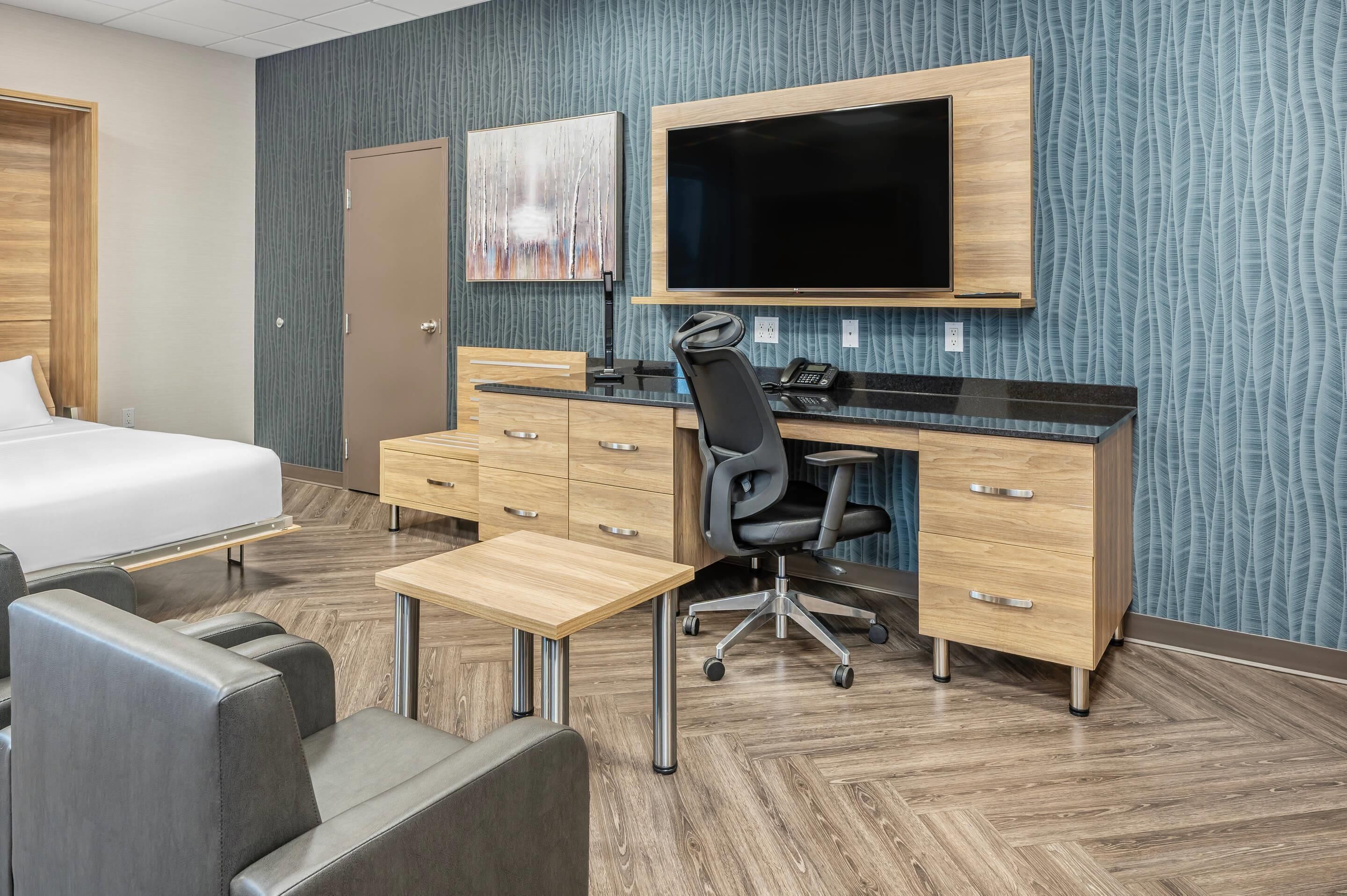 Een hotelkamer met een bed, een bureau met stoel, een flatscreen-tv en een houten dressoir.