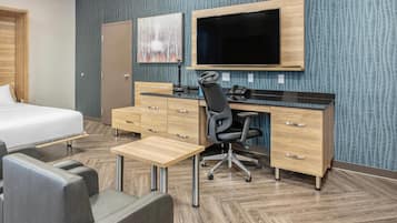 Een hotelkamer met een bed, een bureau met stoel, een flatscreen-tv en een houten dressoir.