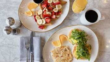 Un desayuno con dos platos de comida, un vaso de jugo de naranja y una taza de café.