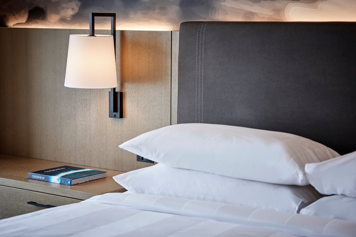 A neatly made bed with white linens, a bedside lamp, and a book titled "Overview" on the nightstand.